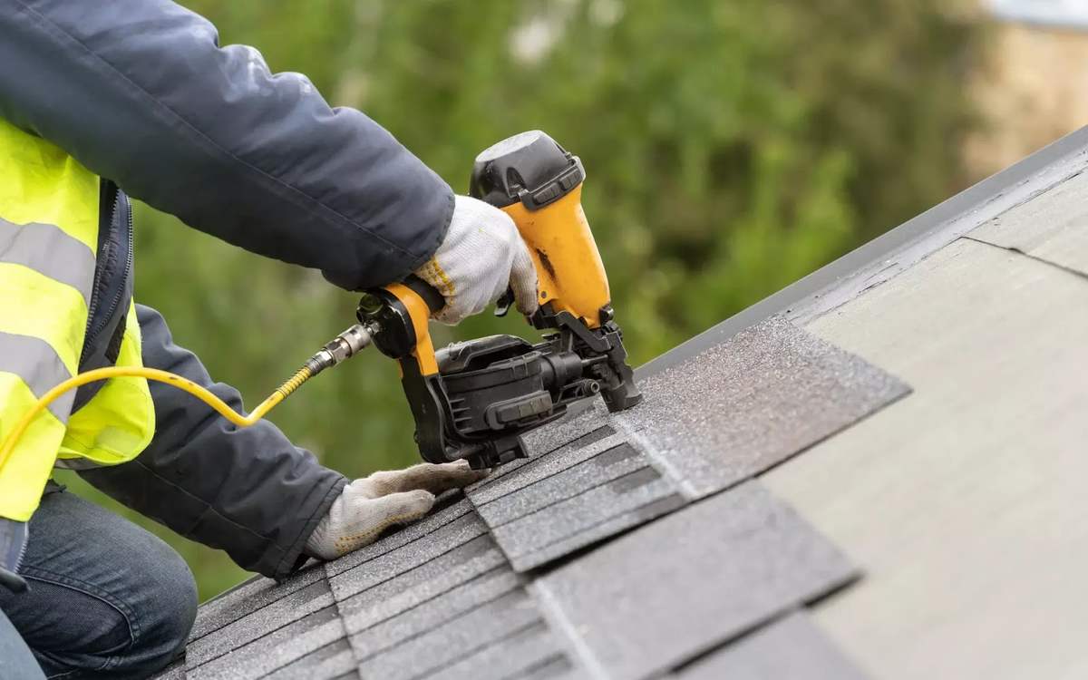 Roofer fastening replacement asphalt shingles with a nail gun during a repair